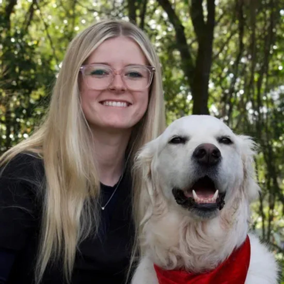 Blonde woman with glasses posing with a golden retriever outdoors