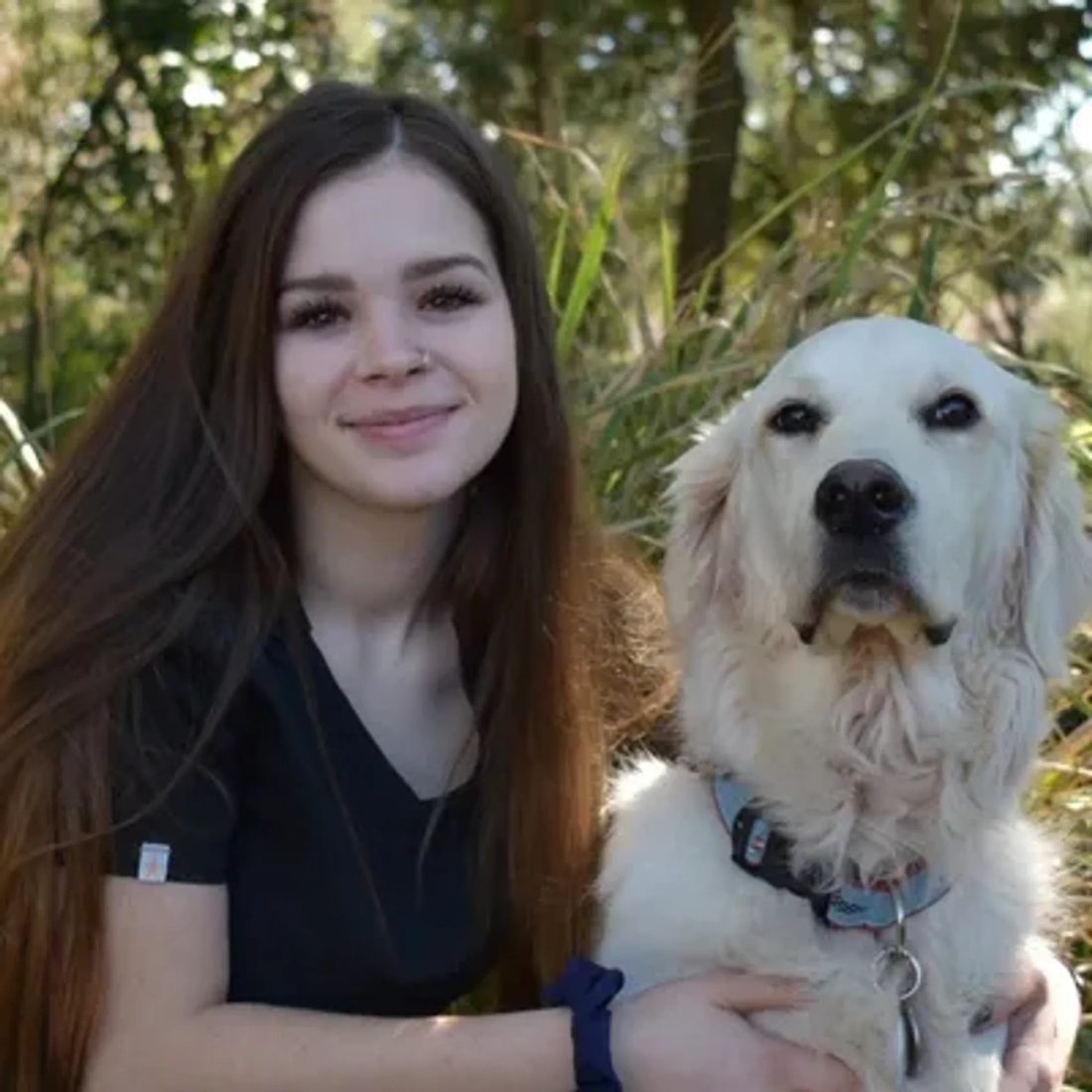 Brunette woman smiling with a golden retriever in a grassy area