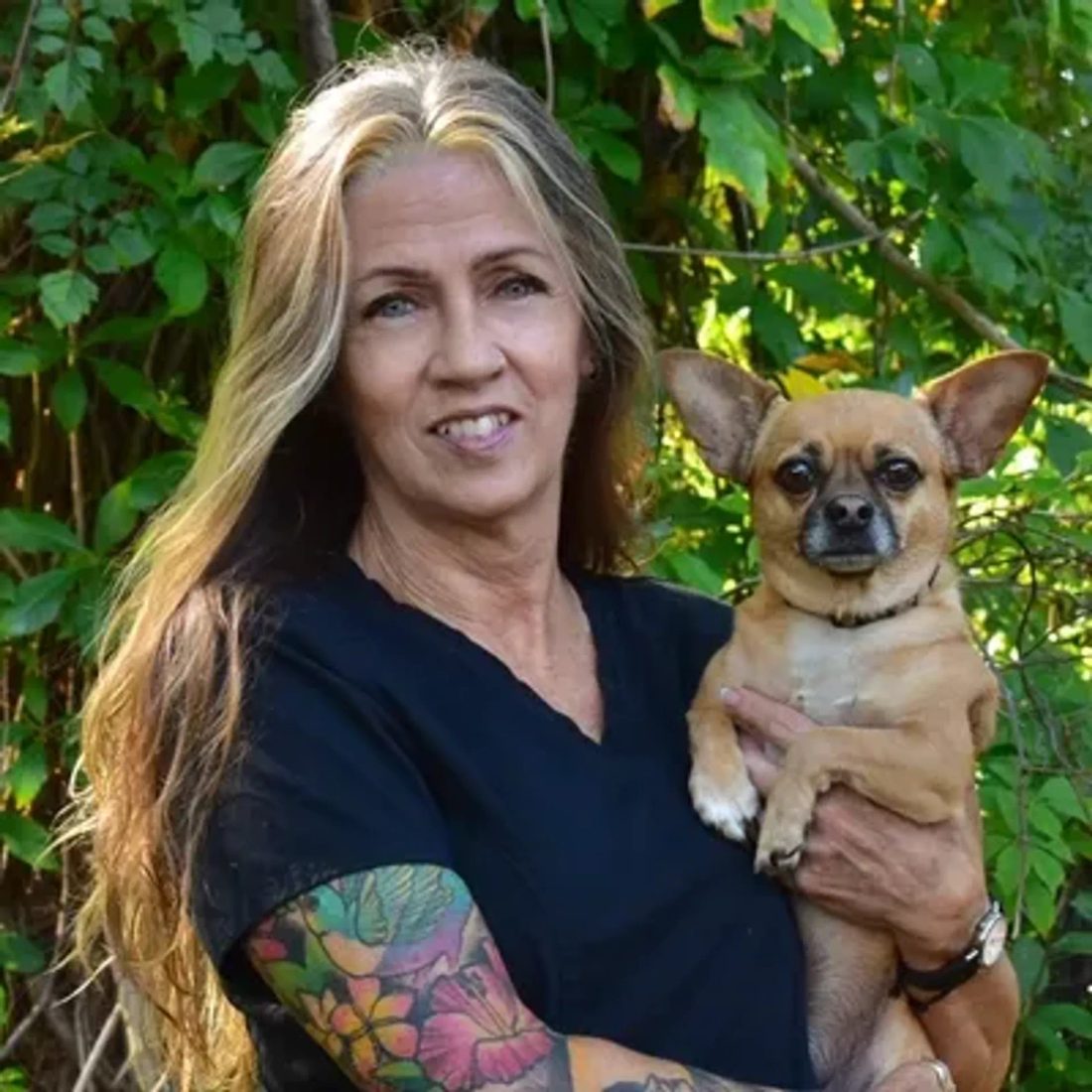 Woman with tattooed arm holding a small chihuahua outdoors